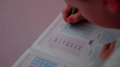 Child practicing math exercises with green pencil, writing on graph paper Stock Footage 332911532