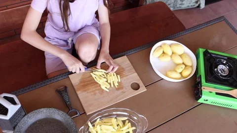 Child prepares fresh fries using potatoes in outdoor kitchen setup Stock Footage 297359360