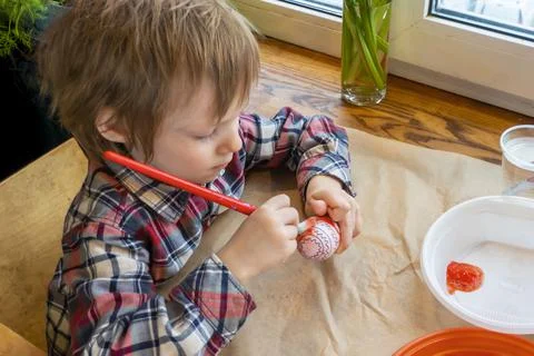 The child preparing for Easter. Paint eggs. Red paint egg. Stock Photos