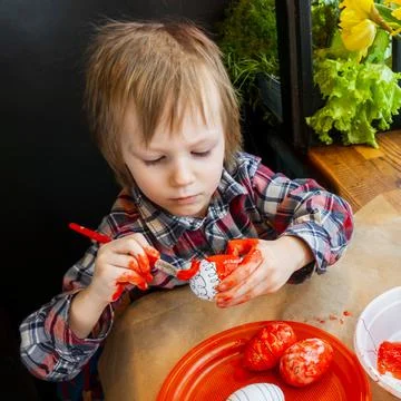 The child preparing for Easter. Paint eggs. Red paint egg. Stock Photos