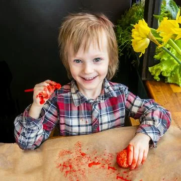 The child preparing for Easter. Paint eggs. Red paint egg. Stock Photos