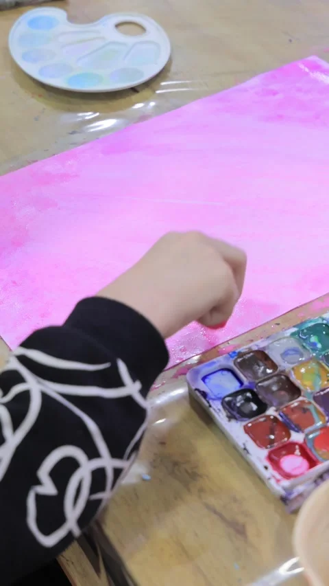 Child preparing watercolor palette while creating a pink background on canvas Stock Footage 322040580