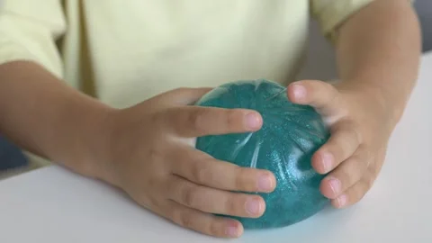 Child presses glittery turquoise squishy character toy closeup at table during Stock Footage 345653911