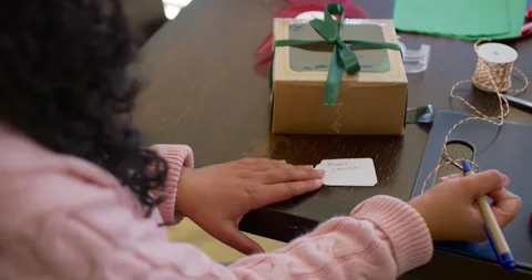 Child is pressing tag to steady it, is writing Christmas label on table near Stock Footage 344227727