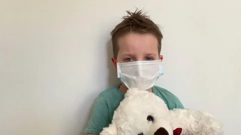 A child in a protective mask sits with a Teddy bear, at home in quarantine Stock Footage 127513963