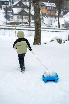 Child pulling blue sled with snow-covered rocks in Spindleruv Mlyn winter Stock Photos