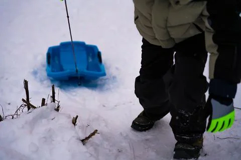 Child pulling blue sled through snow in winter outdoor scene Stock Photos