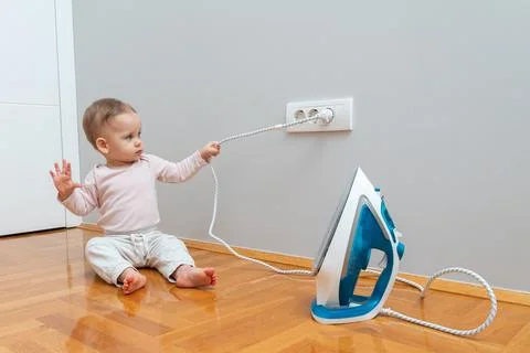 The child pulls the electrical plug out of the socket and turns off the iron Stock Photos