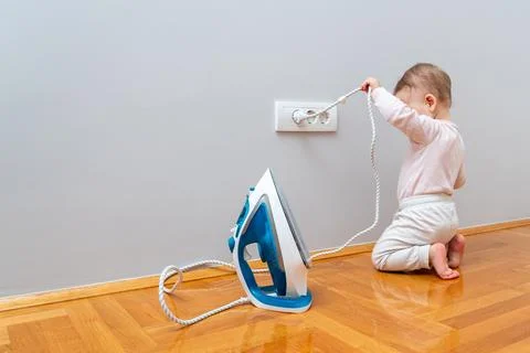 The child pulls the electrical plug out of the socket to let the iron cool down. Stock Photos