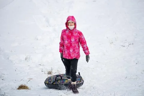 Child pulls an inflatable donut sled on a snowy winter hill. Stock Photos