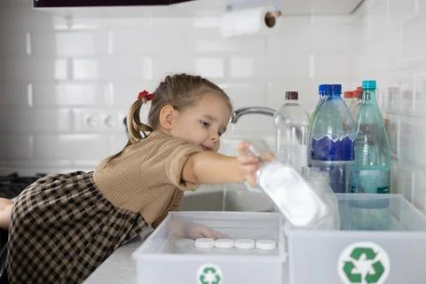 A child pulls a small hand with a plastic bottle to put it in a recycling box. A Stock Photos