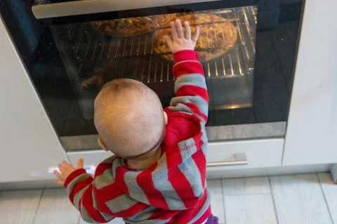 Child pushing at active oven. Stock Photos