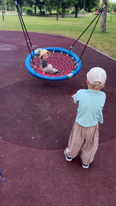 Child pushing playground nest swing with sister inside. Family activity Stock Footage 338055140
