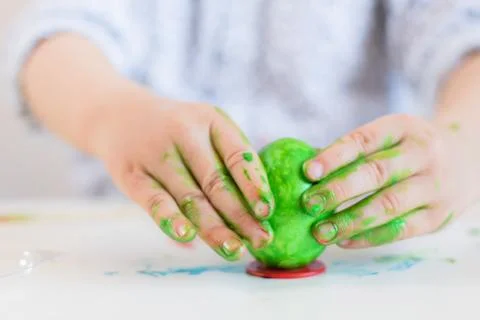 A child puts a green Easter egg on a stand with his hands stained with paint  Stock Photos