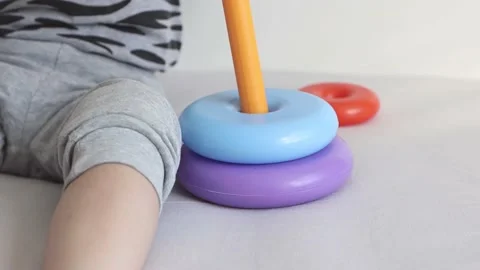 The child puts on the rings of the multi-colored pyramid on the base close-up. Video stock 157128357