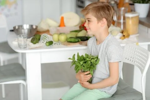 The child puts vegetables on the table and prepares a salad Stock Photos