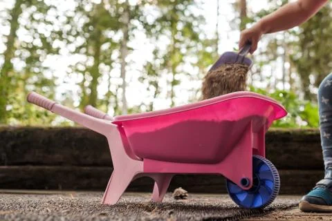 Child putting sas in plastic pink toy wheelbarrow Stock Photos