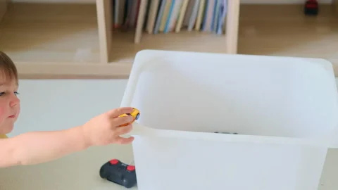 The child is putting the toys back in the box after playing. Kid toddler boy Stock Footage 341857413
