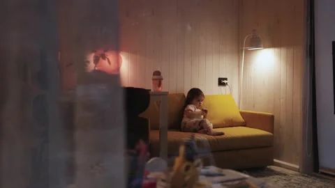 Child on a quiet evening on a yellow sofa watching TV before going to bed at Stock Footage 308922925