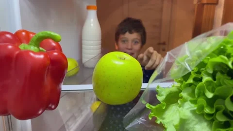 Child reaches for apple in fridge while surrounded by vegetables and milk Stock Footage 324522988
