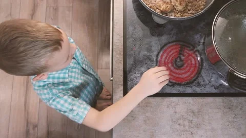 Child reaches for hot electric stove on kitchen. Kid burn danger Stock Footage