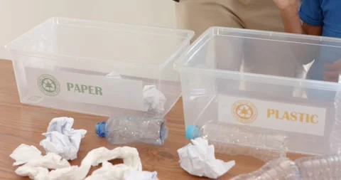 Child reaching is placing paper into PAPER bin, adult is picking PLASTIC bottle Stock Footage 343838147
