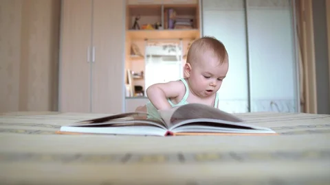 Child read a book lying on the bed. Baby turns the pages. Development of a Stock Footage 128208074