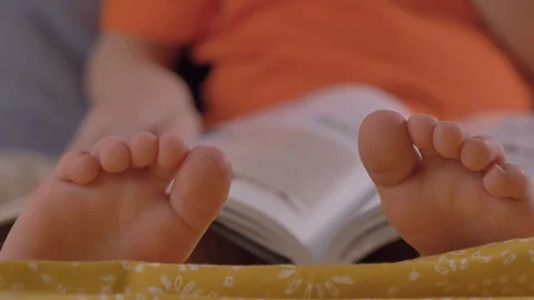 Child reading book, flips a pages, focus on feets, closeup shot Stock Footage 125394331