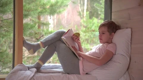 The child reads and eats an apple appetizingly. The boy settled down comfortably Stock Footage 165540789