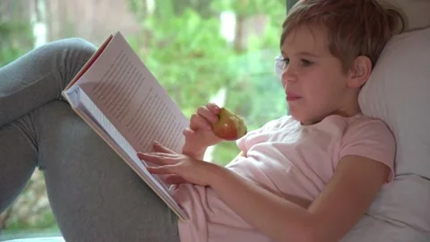 The child reads, laughs and eats an apple appetizingly. The boy settled down Stock Footage 165715090