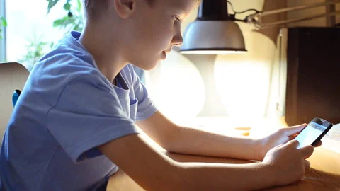 The child reads from the screen of the smartphone sitting at the table Stock Footage
