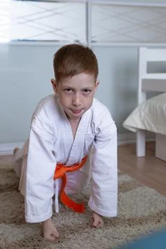 Child red-haired boy is engaged in karate, training push-ups at home in the f Stock Photos