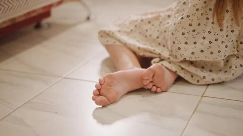 Child relaxes on tiled surface. Child comfortably seated with sunlight on dress Stock Footage 347326120