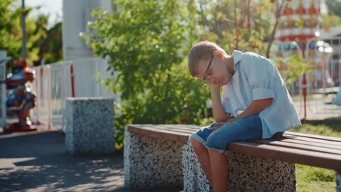 Child relaxing under trees on sunny afternoon. Pensive young male seated on park Stock Footage 335314970