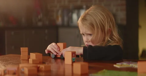 Child responds someone emotionally while playing by the table with wooden blocks Stock Footage 234521881