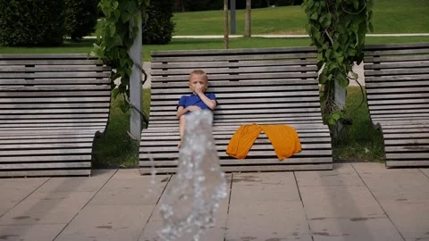 A child is resting on a bench after active games in the fountain in summer. Stock Footage 295192174
