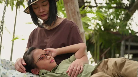 Child resting on mother's lap while swinging gently on wooden swing Stock Footage 306746429