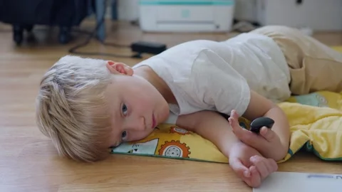 Child resting peacefully, Young boy relaxes on vibrant blanket surface, Light Vidéo 321197472