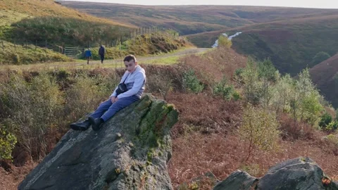 A child rests on a huge boulder, deep in thought. Aerial footage pans aroun.. Vidéo 254161175
