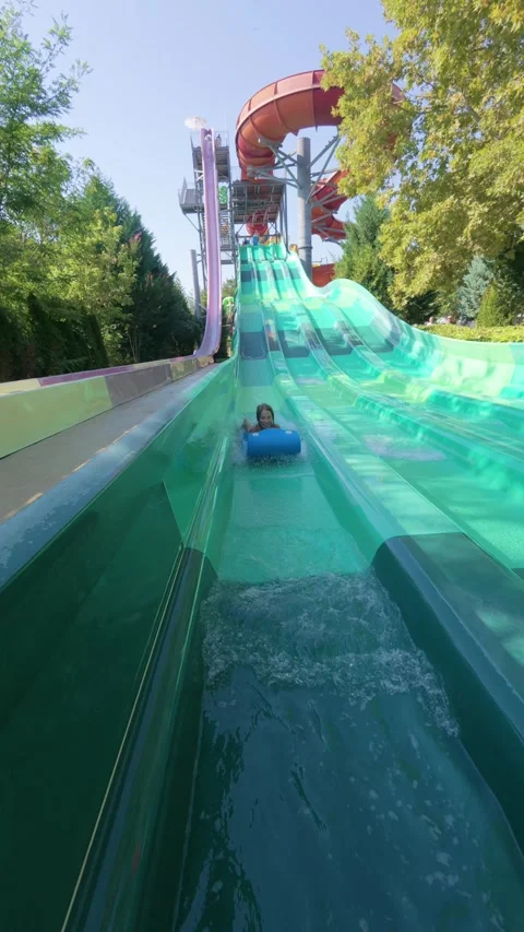 Child riding down a tall multi-lane water slide on a blue mat at a water park Stock Footage 316403635