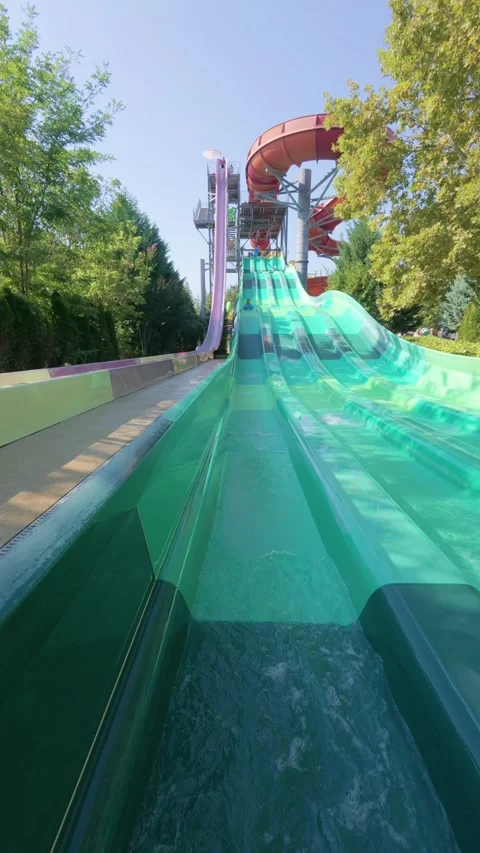 Child riding down a tall multi-lane water slide on a blue mat at a water park Stock Footage 316403731