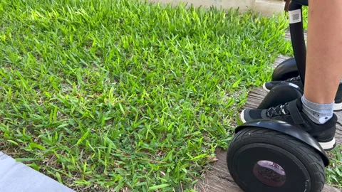 Child riding hoverboard from grass to tile path, close up, 4K30 Video stock 331196293