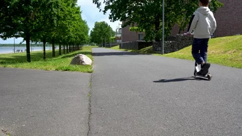 Child Riding Scooter on Lakeside Path in Summer Park Stock Footage 338251329