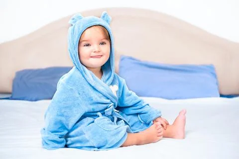 A child in a robe sits on the bed Stock Photos