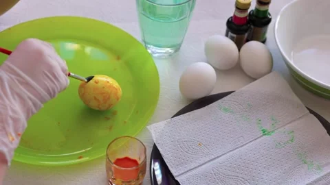 Child rolling hand-painted Easter egg on plate with brush, creating patterns Stock Footage 303674516