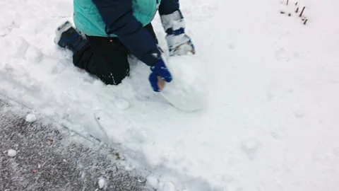 Child rolling large snowball while building snowman outdoors in snowy winter Stock Footage 296061060