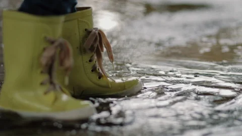 A child in rubber boots stands in a puddle of water in the rain of his feet Stock Footage 121290178