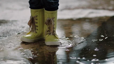 A child in rubber boots stands in a puddle of water in the rain of his feet Stock Footage 121336292