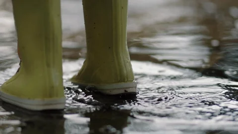 A child in rubber boots stands in a puddle of water in the rain of his feet Stock Footage 121360559