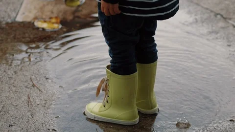 A child in rubber boots stands in a puddle of water in the rain of his feet Stock Footage 121373560